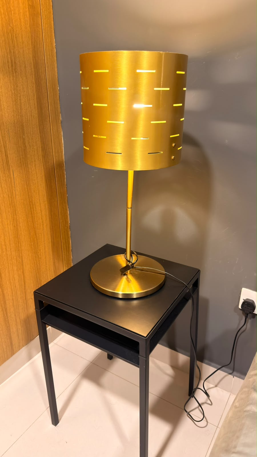 Gold table lamp with perforated drum shade on a black side table