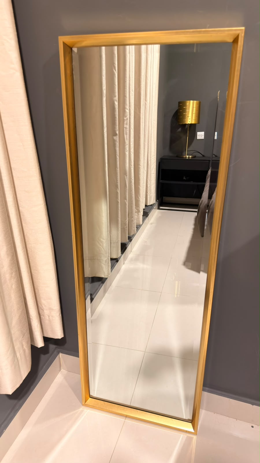 Gold frame full-length mirror leaning against a grey wall