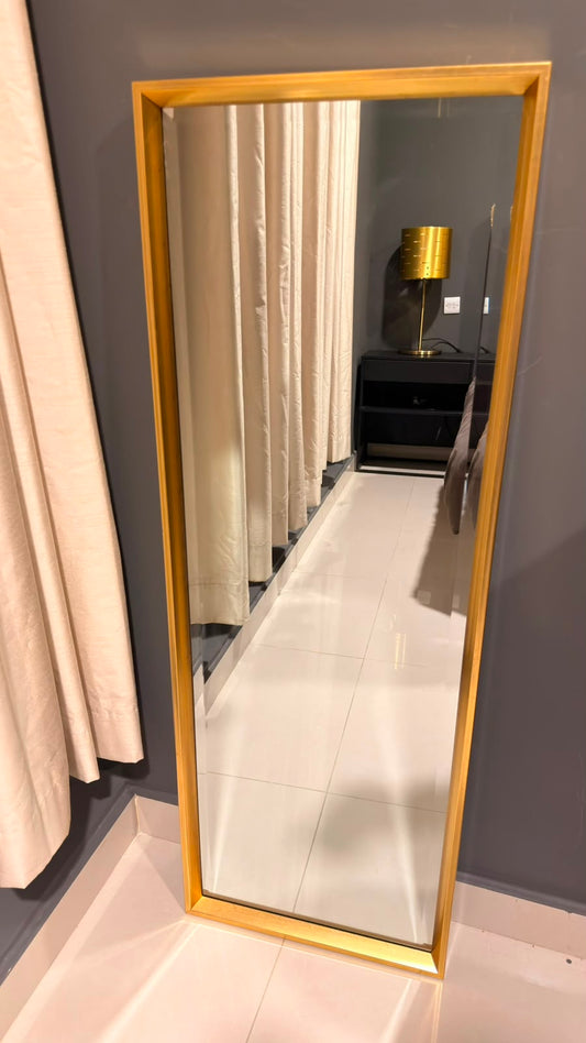 Gold frame full-length mirror leaning against a grey wall
