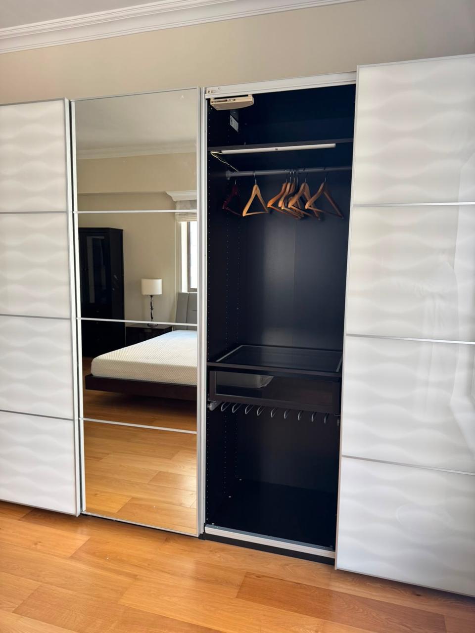 White sliding wardrobe open showing mirror door and interior with hanging rails and shelves