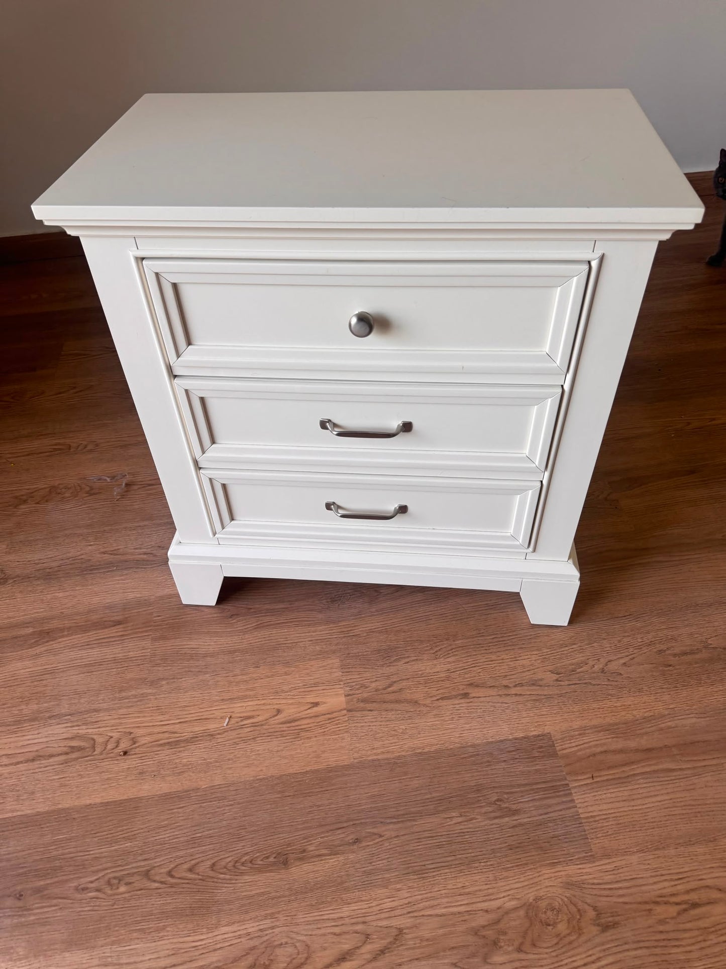 White 3-drawer nightstand with brushed silver hardware on hardwood floor