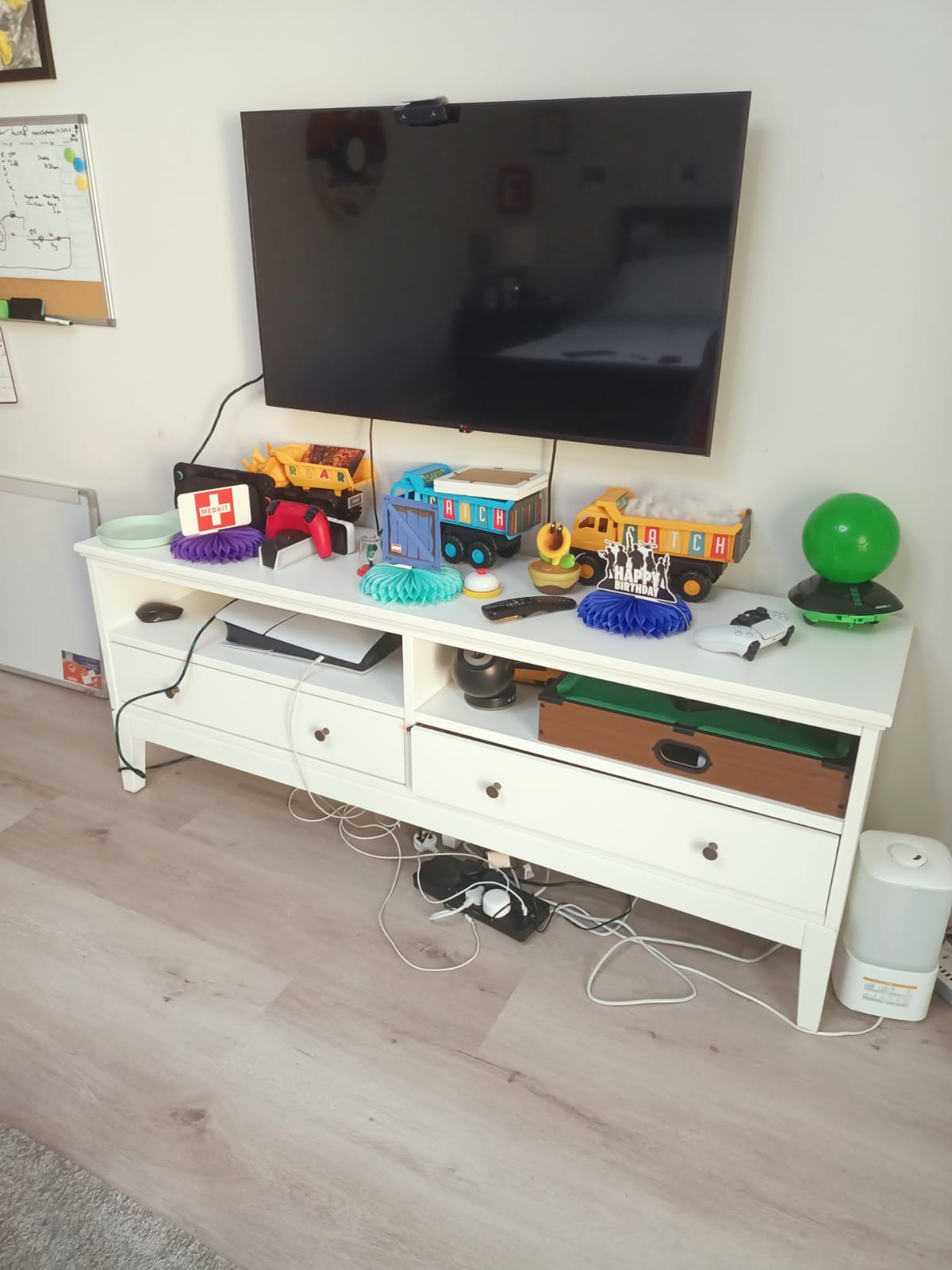Long white TV unit with drawers and open compartments below wall-mounted television