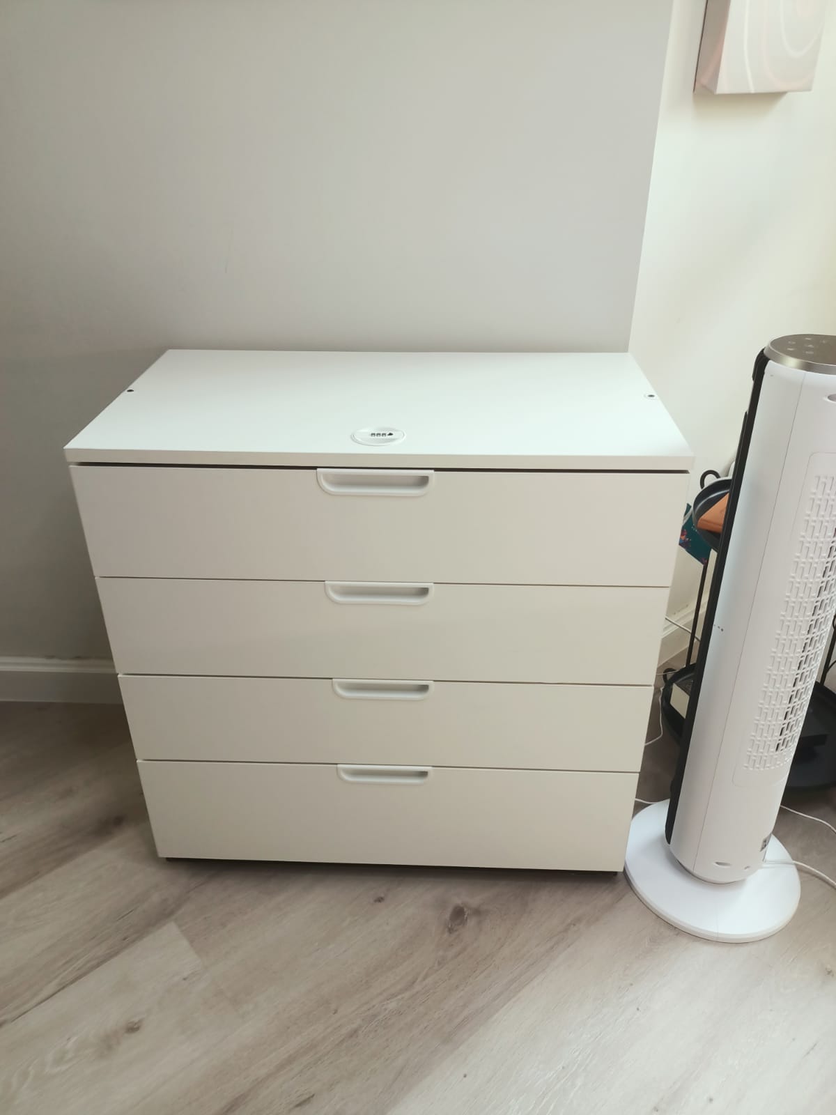 Original photo of low white four-drawer chest beside tower fan