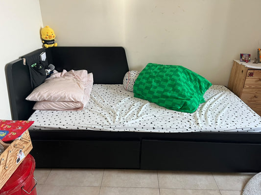 Black low bed frame with corner headboard shown with mattress and bedding